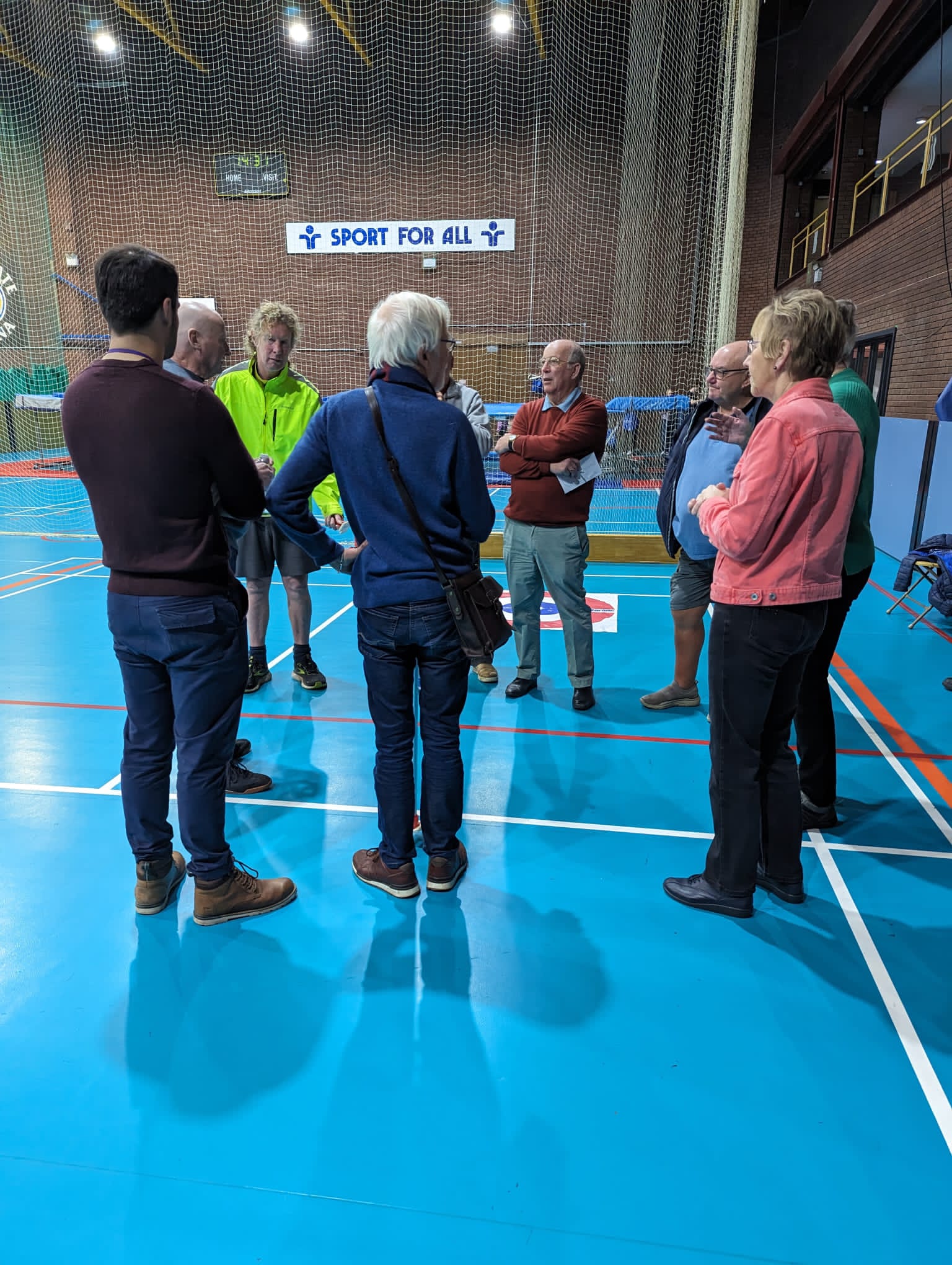 Vision Support Volunteering group stood within a Sports Hall with the wording 'Sport For All' visible in the background.