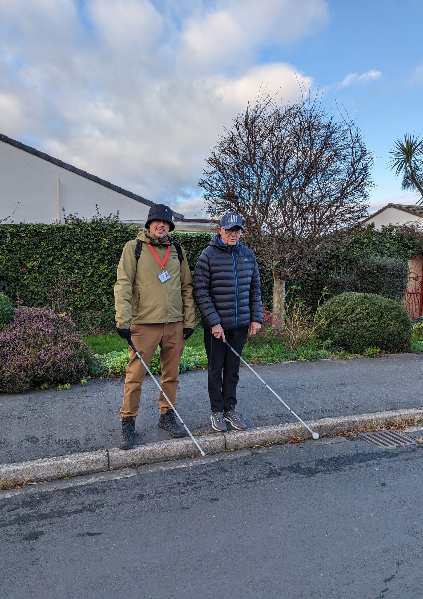 Two People standing on pavement both with guide sticks to help them