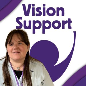 with long brown hair wearing a light-coloured blouse and a purple lanyard stands in front of a white background with the large purple Vision Support logo behind her, featuring the words “Vision Support” above a circle held within a curved arc shape.
