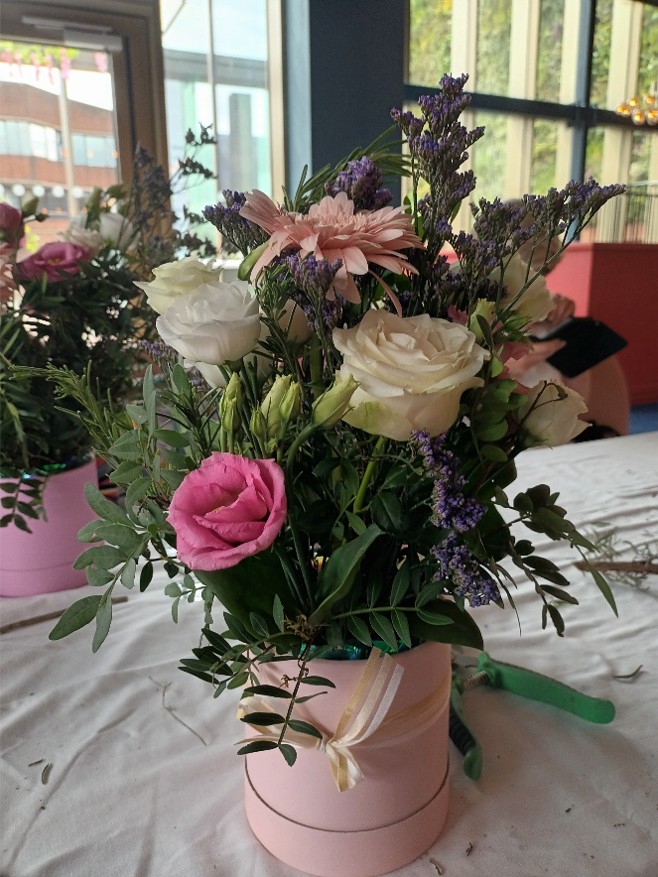 Pink and white flowers and foliage in a pink flower box on a table
